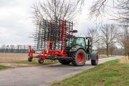 Traktor s neseným příslušenstvím na cestě mezi poli.