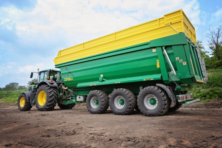 Traktor John Deere táhne velkokapacitní zeleno-žlutý přívěs Curtarelli určený k přepravě zemědělských plodin.