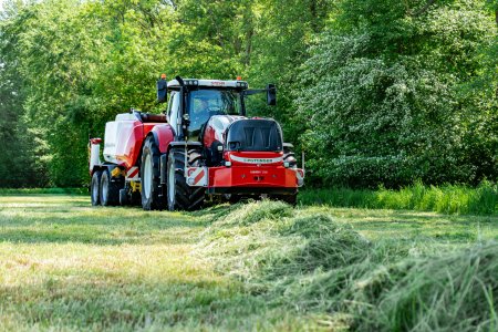 Traktor Steyr s návěsem Pöttinger Jumbo sbírá posečenou píci z řádku na louce.