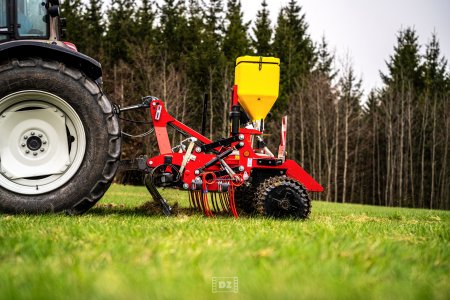 Traktor s výsevním strojem a žlutým zásobníkem na osivo provádí regeneraci travního porostu.