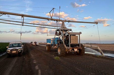 Na fotografii probíhá obsluha a kontrola pivotového závlahového systému, který čerpá vodu z kanálu pomocí mobilní motorové jednotky umístěné přímo na podvozku pivotu.