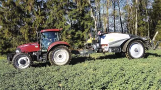 Červený traktor Case IH s postřikovačem u stromů