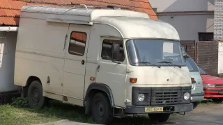 Starší světlý skříňový automobil AVIA zaparkovaný u domu.