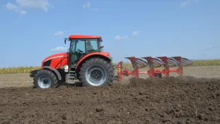 Červený traktor s pluhem SUKOV při orbě