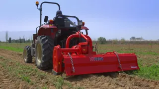 Červený traktor Yanmar s půdním nářadím na poli