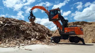 Oranžový manipulátor Develon překládá dřevní štěpku