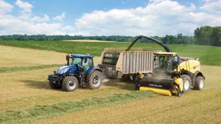 Sklízecí řezačka New Holland sklízí píci vedle traktoru s návěsem.