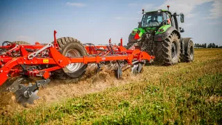 Traktor s červeným kypřičem Kuhn při polní ukázce.