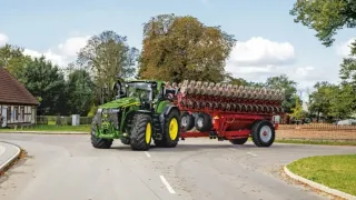 Traktor John Deere táhne zemědělský stroj po silnici