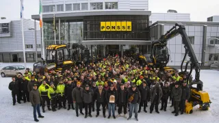 Skupina zaměstnanců před budovou a lesním strojem Ponsse