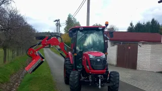 Červený traktor TYM s ramenovou sekačkou u silnice