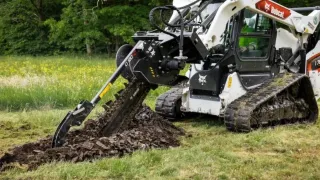 Pásový nakladač Bobcat s rýhovačem hloubí rýhu v travnatém terénu.