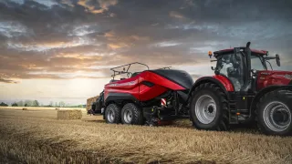 Červený traktor Case IH s lisem na balíky na poli