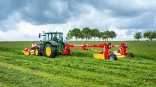 Zelený traktor s žacím strojem Pöttinger na louce