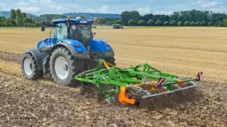 Modrý traktor s připojeným půdozpracujícím strojem na poli