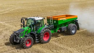 Zelený traktor s rozmetadlem hnojiva na poli