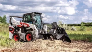 Bílý smykem řízený nakladač Bobcat na louce