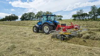Modrý traktor se shrnovačem sena na louce
