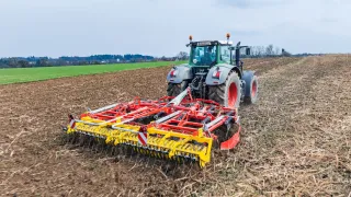 Červený kypřič Pöttinger za traktorem na poli