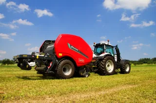 Traktor s červeným lisem Kverneland FastBale na louce.