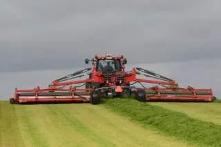 Červený traktor s širokou žací kombinací na louce
