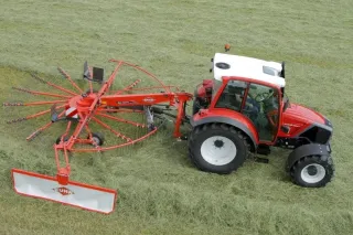 Červený traktor s jednorotorovým shrnovačem Kuhn na louce