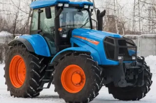 Modrý traktor Agromash se zářivě oranžovými koly na sněhu