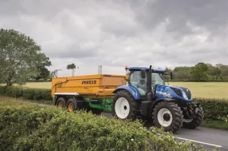 Modrý traktor New Holland se žlutým návěsem na silnici