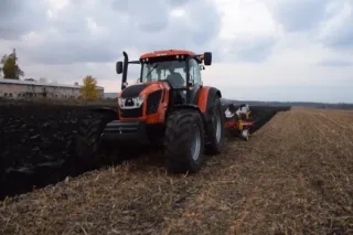 Červený traktor Zetor Crystal oře tmavé pole.