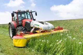 Červený traktor s čelní žací lištou Pöttinger na louce
