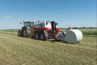 Traktor s lisem Pöttinger a zabaleným balíkem na louce