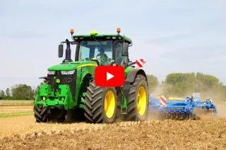 Zelený traktor John Deere s modrým strojem na zpracování půdy.
