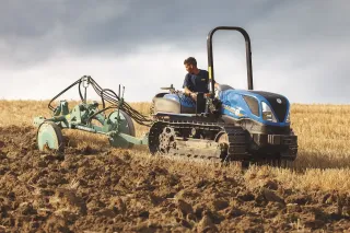 Malý modrý pásový traktor New Holland při práci na poli