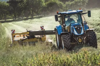 Modrý traktor New Holland T6 při sečení louky