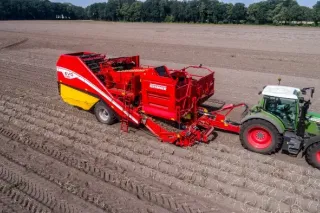 Červený sklízeč Grimme Evo 280 tažený traktorem na poli