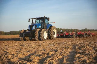 Modrý traktor New Holland T8 s širokým strojem na poli