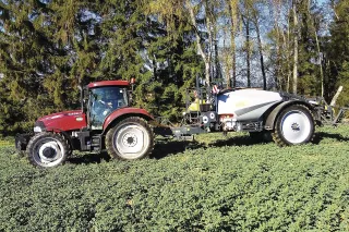 Červený traktor Case IH s postřikovačem u stromů