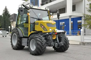 Žlutý elektrický traktor Rigitrac SKE 50 před budovou