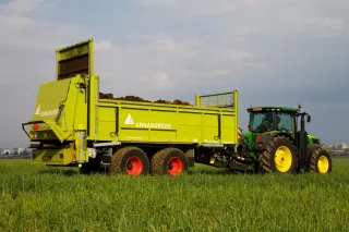 Zelený traktor táhne žlutý návěs Annaburger na poli