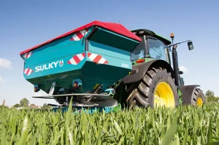 Rozmetadlo Sulky DX W-Control připojené k traktoru na poli
