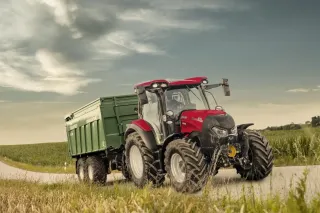 Červený traktor Case IH s velkým zeleným návěsem na cestě