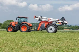 Oranžový traktor Kubota s taženým postřikovačem na louce