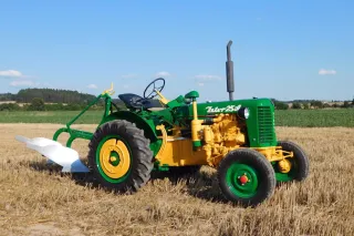 Zrenovovaný zelenožlutý traktor Zetor 25 A s pluhem na poli