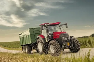Červený traktor Case IH se zeleným návěsem na cestě
