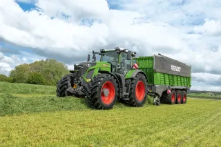 Zelený traktor Fendt s návěsem Tigo na louce