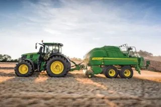 Zelený traktor John Deere s lisem na poli