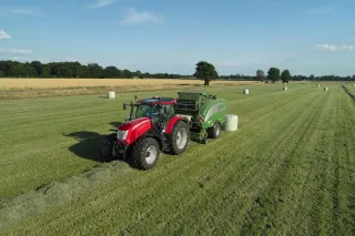 Červený traktor s připojeným zemědělským strojem na louce
