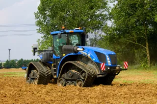 Modrý pásový traktor New Holland při práci na poli