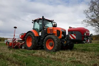 Oranžový traktor Kubota se secím strojem na poli