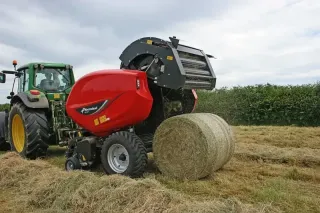 Traktor s červeným lisem Kverneland 6500F na louce